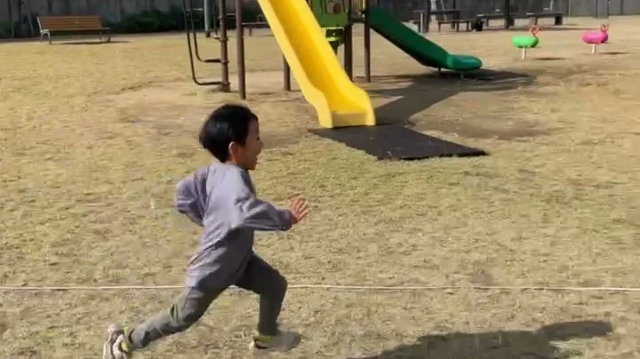 公園の芝生で、大きく腕を振って走る子ども